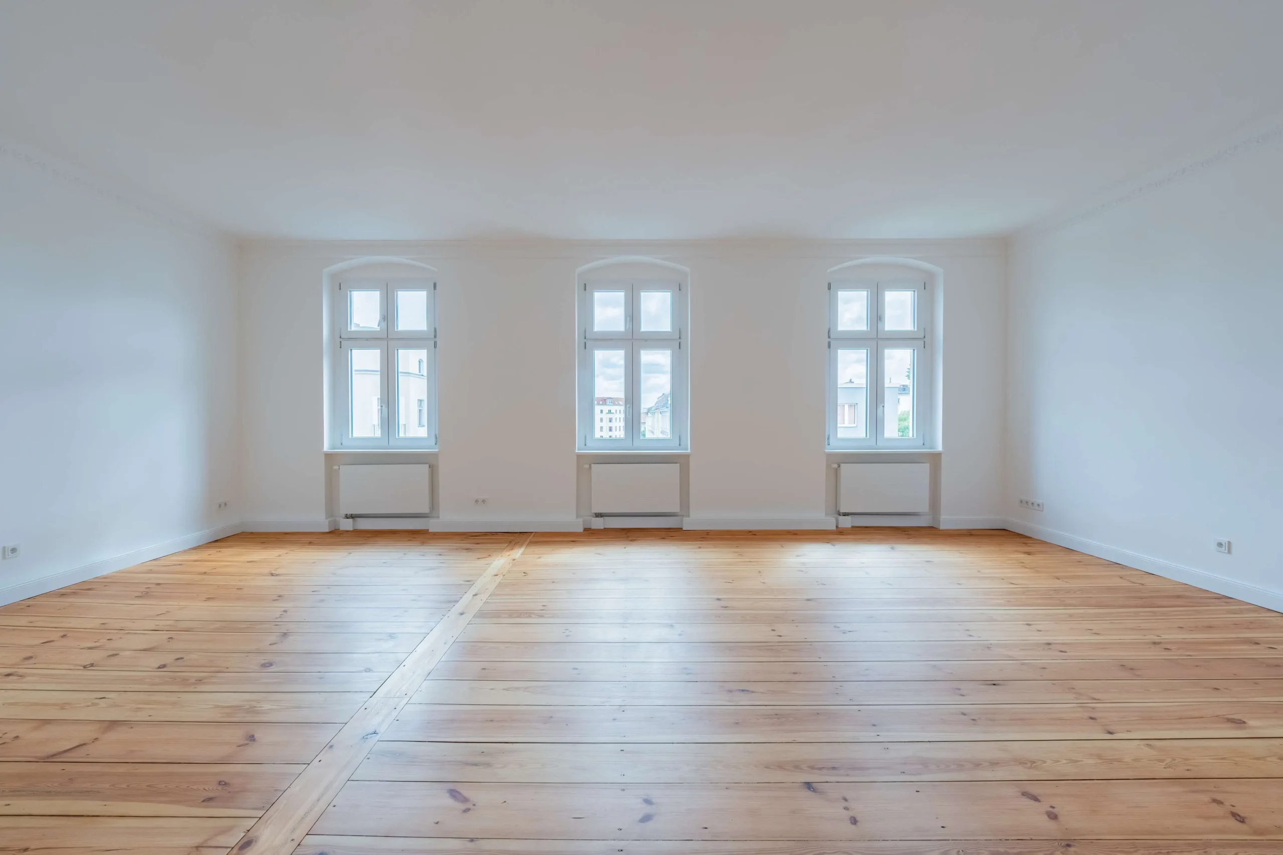 Wohnzimmer der sanierten Altbauwohnung Perleberger Straße 28 in Berlin mit drei Bogenfenstern und Dielenboden